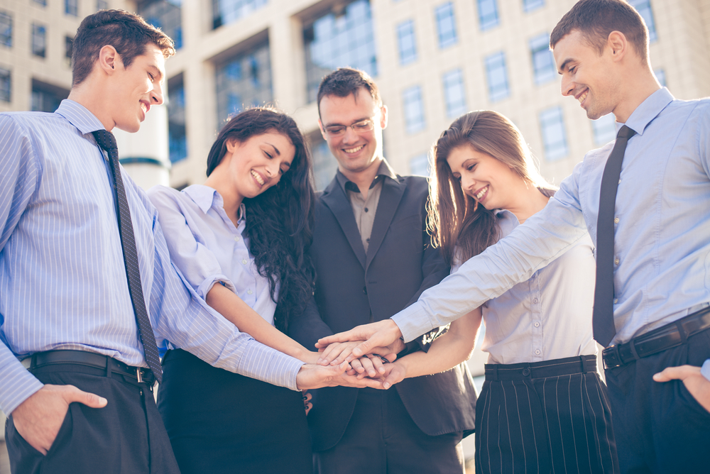 Group of young business people standing in front of the company with folded hands, motivating for new business wins.